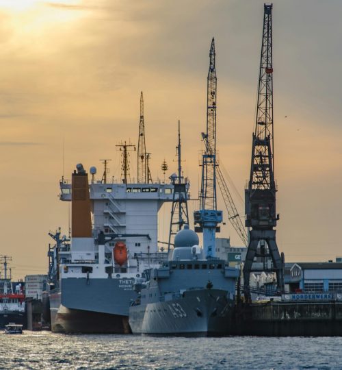 Cargo port scene with ships and cranes at sunset, showcasing industrial and maritime activity.